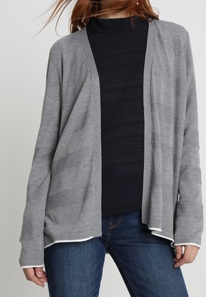 Cardigan grigio chiaro a maniche lunghe realizzato in un tessuto morbido, con apertura frontale e una sottile texture a coste. Abbinato a una maglia nera e jeans blu.