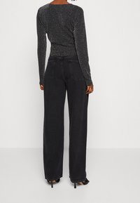 Svart, glittrande långärmad topp med figursydd design och rund halsringning, tillsammans med högmidjade, vida svarta jeans.