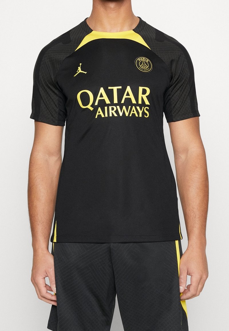 Jersey deportivo negro con detalles y logotipo en amarillo, que presenta un patrón texturizado y mangas cortas. "QATAR AIRWAYS" impreso de forma prominente en amarillo.