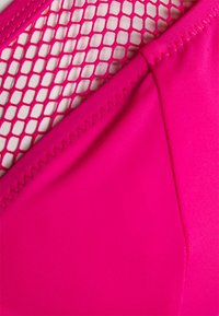 Tecido de fato de banho rosa com um painel de malha aberta texturizada. O detalhe das costuras suaves ao longo das bordas realça a integridade do design.