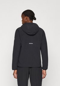 Giacca in fleece nera con cappuccio, maniche lunghe, colletto alto e logo sulla schiena. Texture liscia, vestibilità casual e design leggero.