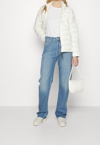 Biała kurtka puchowa, jasnoniebieskie dżinsy, biała koszulka, jasne buty i mała biała torebka na łańcuszku.