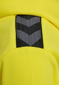 Helle gelbe Stoff mit strukturierter Oberfläche, der ein schwarzes Patch mit einem Chevron-Muster aufweist. Das Design umfasst glatte, abgerundete Kanten.