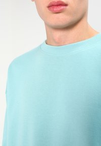 Sudadera de cuello redondo en azul claro, hecha de una tela suave, con un cuello acanalado y un diseño minimalista, de textura lisa y sin patrones visibles.