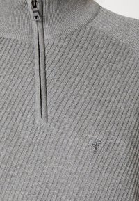 Grauer Reißverschluss-Pullover mit gerippter Textur, hohem Kragen und besticktem Logo auf der Brust. Verfügt über passende Reißverschlussdetails.