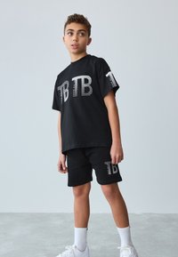 Sort bomulds T-shirt og shorts sæt med hvidt stribet "TB" print. Outfittet har en afslappet pasform og er sammensat med hvide sneakers og sokker.