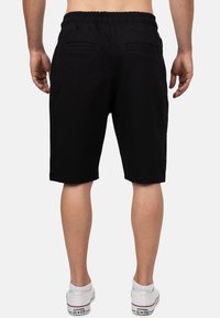 Shorts noirs avec une taille élastique, deux poches arrière et une coupe décontractée. Fabriqués en tissu doux, ils présentent des accents contrastants sur les côtés.
