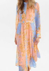 Robe boutonnée à manches longues avec motif floral pêche et bleu et motif bambou, portée avec un pantalon assorti, ceinturée à la taille.