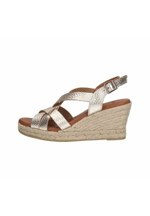 Wedge sandals with metallic gold crisscross straps, brown footbed, and woven jute sole. Adjustable ankle strap with a silver buckle.