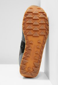 Sneaker outsole in grey and black with a rubber orange traction pattern. Features triangular treads for grip and a curved silhouette for flexibility.
