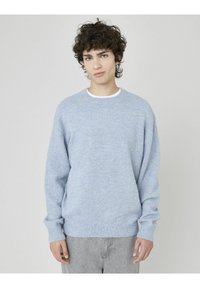 Pull en bleu clair à col rond avec une texture douce, coupe décontractée, et bords-côtes aux poignets et à l'ourlet. Assorti à un jean gris clair.