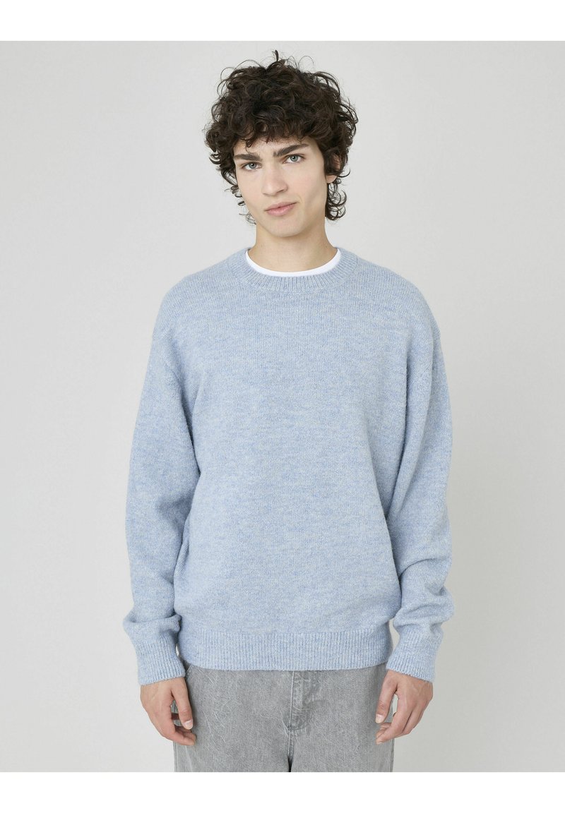 Pull en bleu clair à col rond avec une texture douce, coupe décontractée, et bords-côtes aux poignets et à l'ourlet. Assorti à un jean gris clair.