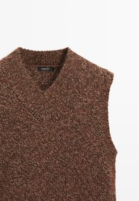 Maglione senza maniche marrone a maglia con scollo a V, caratterizzato da una trama testurizzata e un'etichetta sul colletto.