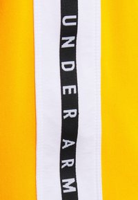 Gult tyg med en vit rand och svart text "UNDER ARM". Slät textur och tydlig kontrast mellan färgerna.