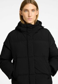 Sort pufferjakke med høj krave og snørehætte. Har et quiltet design, frontlommer og lynlåslukning. Mat finish.