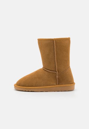 Tan suede ankle boot with seamless design, rounded toe, and soft texture. Features a tan rubber sole and minimal stitching accents.