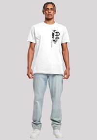 Vit bomull t-shirt med svarta tryckta grafiker, inklusive logotyper och text, rundad halsringning och korta ärmar, tillsammans med ljusblå jeans.