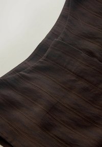 Primo piano di un tessuto marrone scuro a righe verticali con un dettaglio di cucitura strutturata su uno sfondo chiaro.