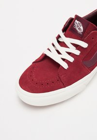 Bordeaux ruskindsneaker med hvide snørebånd, med en tonet logopatch, perforerede detaljer på tåen og en tekstureret gummisål.