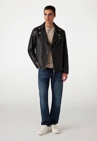 Czarna skórzana kurtka motocyklowa z srebrnymi zamkami błyskawicznymi, w połączeniu z beżowym t-shirtem, niebieskimi dżinsami i białymi trampkami. Prosty krój, gładka faktura.