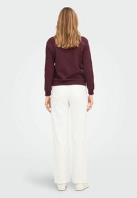 Felpa color bordeaux con maniche lunghe, polsini a coste e orlo arrotondato, abbinata a pantaloni bianchi a gamba larga e sneakers bianchi.