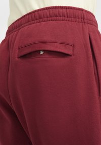 Maroon sweatpants featuring a textured fabric, elastic waistband, and a back pocket with a snap closure.