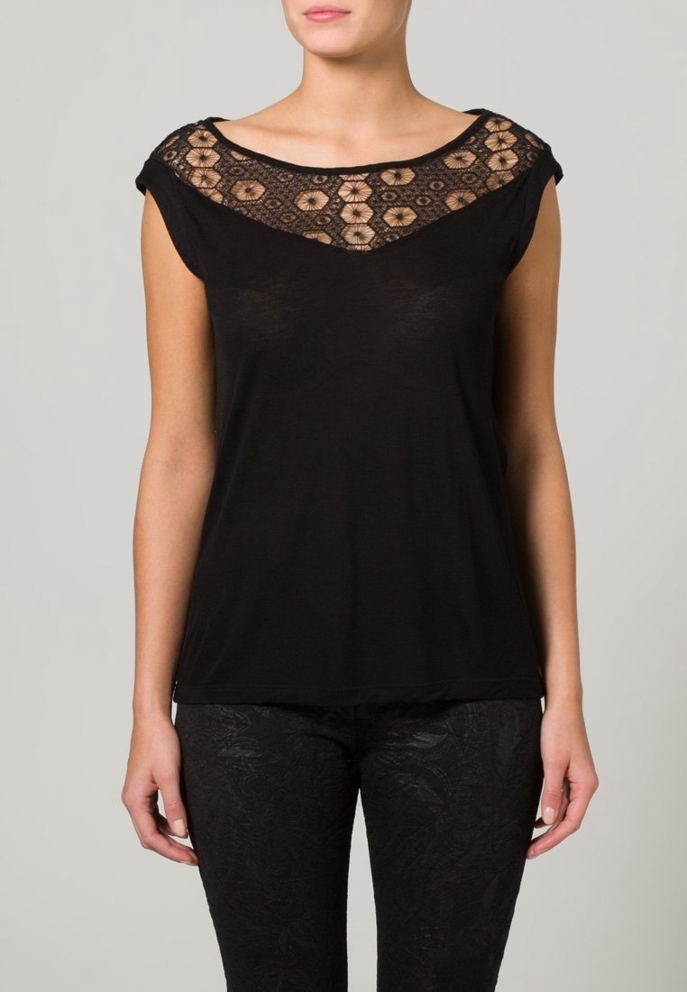 Lyhythihainen musta paita, jossa on pitsiyksityiskohta kaula-aukossa ja kukkakuosi, rento istuvuus, yhdistettynä teksturoituihin mustiin housuihin.