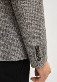 Grau strukturierter Blazerärmel mit vier dunklen Knöpfen, dezentem Muster und sauberer Nahtführung. Maßgeschneidertes Design, weicher Stoff.