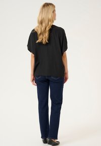 Svart löst sittande topp med korta ärmar, i kombination med mörkblå raka jeans och svarta ballerinas, sedd bakifrån.