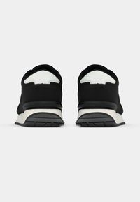 Ζευγάρι μαύρα και άσπρα αθλητικά παπούτσια, εμφανιζόμενα από πίσω, σε λευκό φόντο.