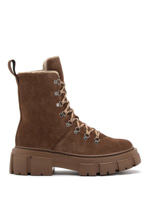 Brown suede ankle boots with a thick, textured sole, featuring metal eyelets, lace-up design, and a faux fur lining at the collar.