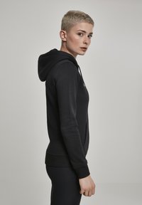 Black hoodie made of soft material, featuring a front pocket, drawstring hood, and ribbed cuffs. Model shown in a side profile.