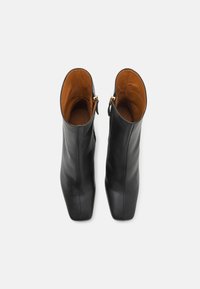 Botas de cuero negras hasta el tobillo con un acabado suave, diseño de punta cuadrada y un interior de cuero marrón. Presentan un detalle de cremallera dorada en el lateral.