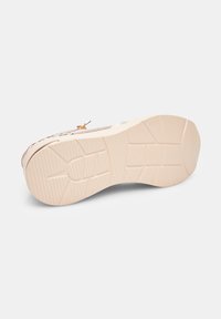 Semelle de sneaker beige clair avec caoutchouc texturé, présentant une forme arrondie, des rainures horizontales et verticales, et un petit logo près du talon.