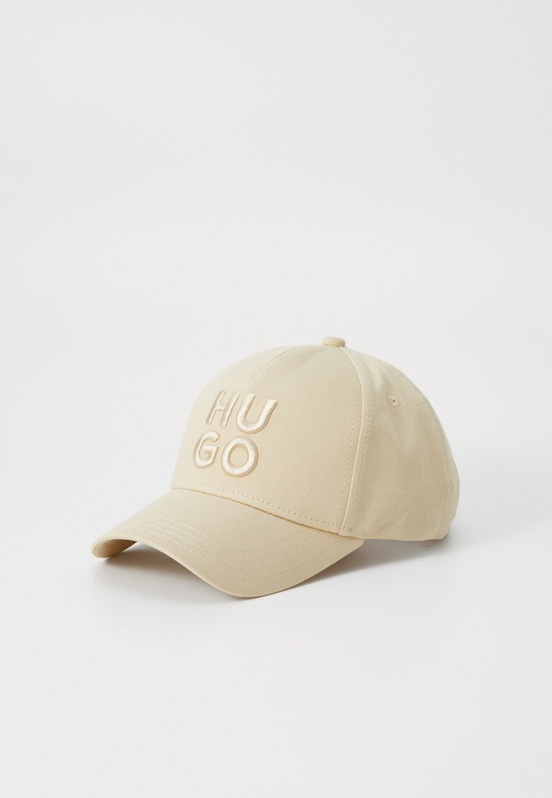 Beige baseball cap with an embroidered "HUGO" logo. Features a curved brim and a textured fabric. Adjustable strap at the back.