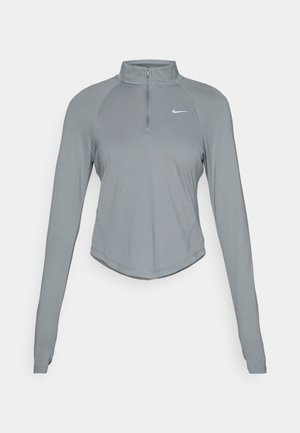 Grå langærmet træningstop med kvart lynlås og hul til tommel, der har et lille hvidt Nike-logo på venstre bryst.