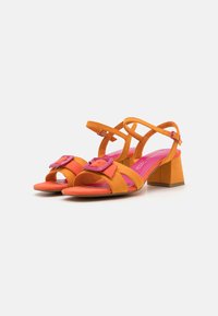 Sandali con tacco arancioni e rosa, con cinturini incrociati e una fibbia quadrata sul davanti. Presentano un tacco a blocco e una texture in camoscio.