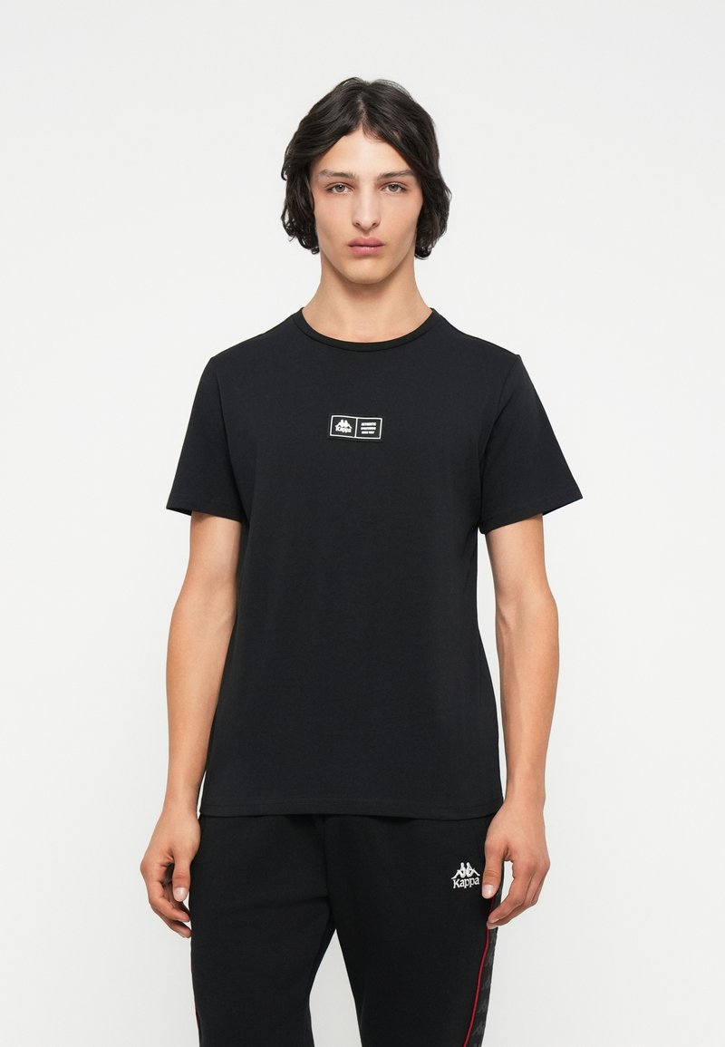 Czarny bawełniany t-shirt z krótkim rękawem, okrągłym dekoltem, z małą naszywką z logo na piersi. Ogólnie gładka tekstura.