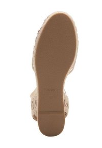 Nude sandal sole featuring textured rubber for grip, a sturdy heel, and a subtle logo imprint on a smooth surface.