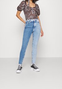 Höga ljusblå denim skinny jeans med en blekt tvätt, i kombination med en leopardmönstrad topp och svarta sneakers. Mjuk textur, åtsittande design.