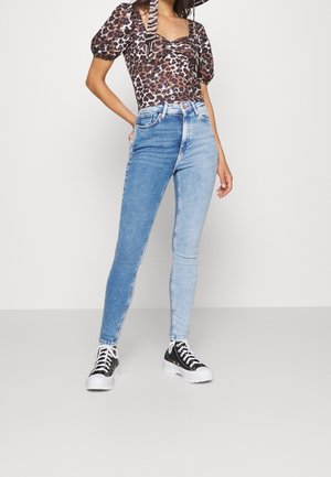Jeans skinny de denim de tiro alto en un azul claro con un acabado desvanecido, combinados con una blusa de estampado de leopardo y zapatillas negras. Textura suave, diseño ajustado.