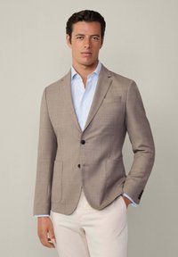 Blazer beige ajusté avec des revers à cran, deux poches avant, fermeture à un bouton, associé à une chemise à carreaux bleu clair.