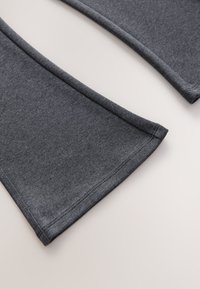 Pantalon en tissu tricoté gris foncé avec ourlets évasés présenté sur une surface claire, montrant des détails de couture soignés.