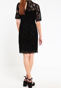 Svart spetsklänning med korta ärmar, med en scalloped nederkant och nyckelhål bakdetalj. Kombinerad med svarta högklackade sandaler.