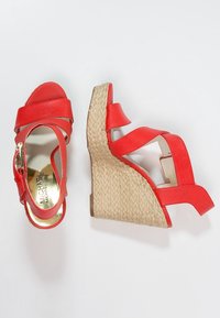 Sandali rossi con zeppa, dotati di cinturini incrociati, realizzati in materiale sintetico testurizzato, con tacco in juta intrecciata. Logo dorato sulla soletta.