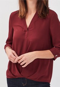 Bourgognefarvet bluse med V-udskæring og 3/4 ærmer. Blødt stof med knyttet kant og dekorative knapdetaljer på ærmerne.