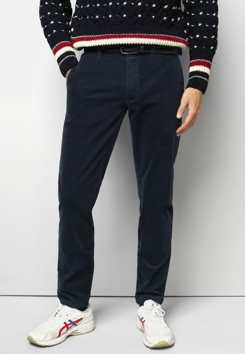Navy blue chinos made from cotton with a slim fit. Features front pockets and a smooth texture, paired with white athletic shoes.