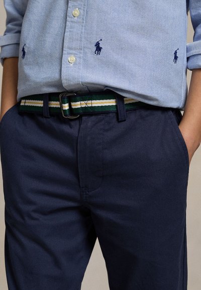 Jasnoniebieska koszula z ciemnoniebieskimi logotypami graczy polo, wsunięta w granatowe spodnie z paskiem w zielone, białe i żółte paski.