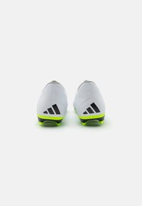 Scarpe da calcio leggere bianche con accenti neri e una suola verde brillante, caratterizzate da un design elegante e lati testurizzati per una migliore aderenza.