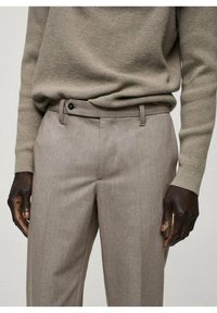 Beige op maat gemaakte broeken met een gladde textuur, een vlakke voorkant en een enkele knoopsluiting. Gecombineerd met een licht gebreid sweater.